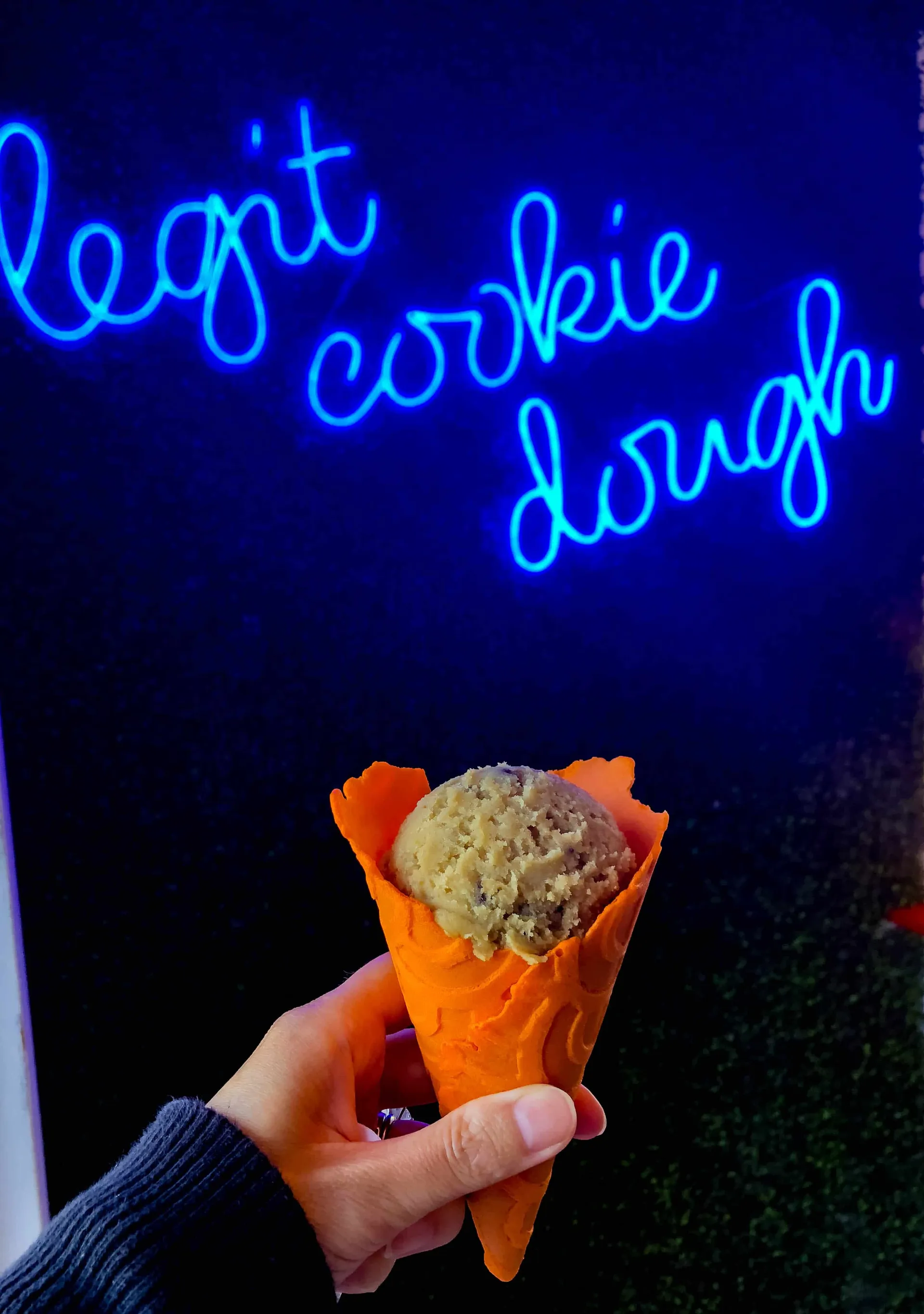 A cookie dough cone from Doughp in front of a neon sign at Pier 39 San Francisco