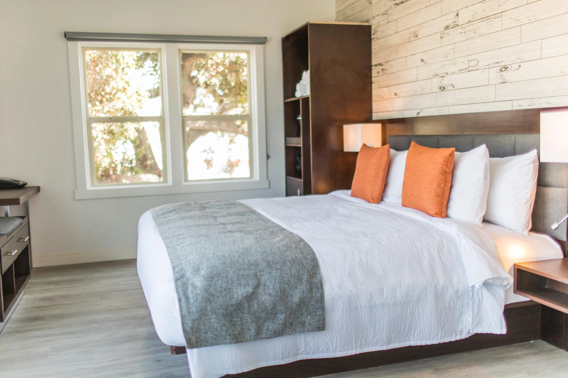 Guestroom with contemporary decor (bed with crisp white sheets, orange throw pillows and a grey blanket across the edge)