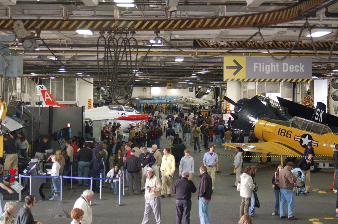 People roam the hangar deck among aircraft at USS Midway Museum.