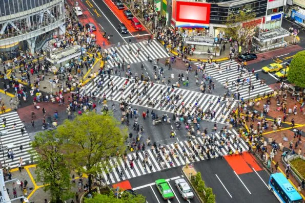 An overhead view of people on the crosswalks of the Shibuya Crossing with traffic stopped in all directions.