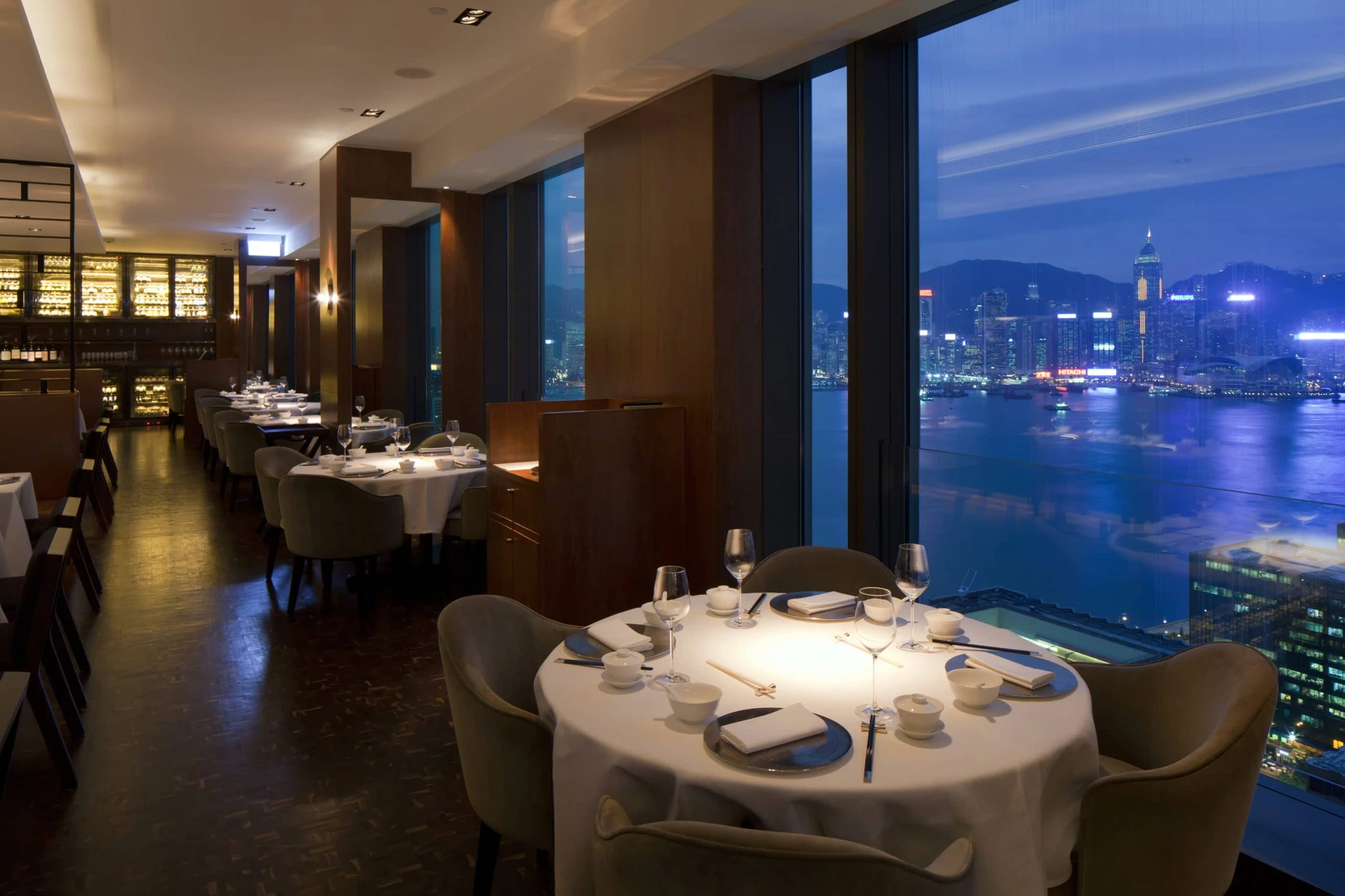 Tables near the windows at Above & Beyond with nighttime panoramic harbour views.