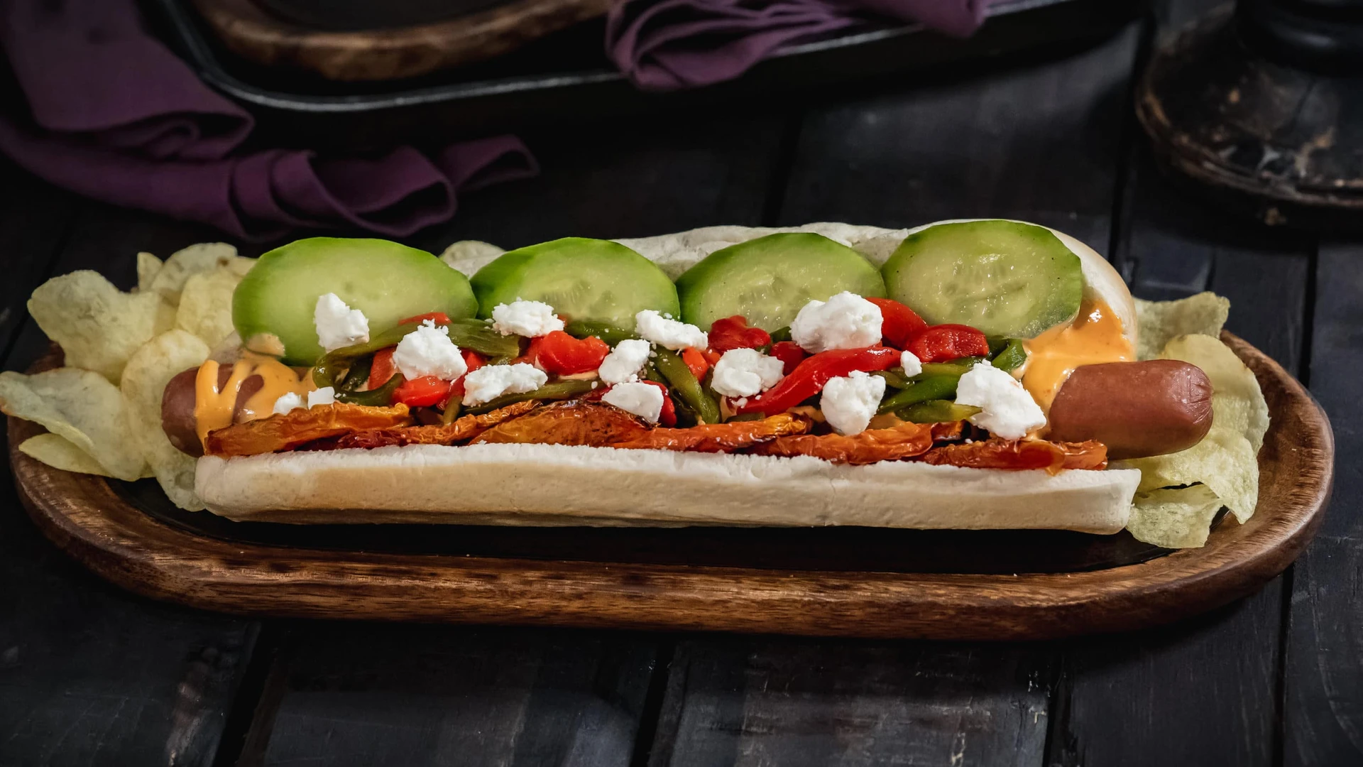 Hades-inspired hot dog with neatly-placed toppings on a wood board.