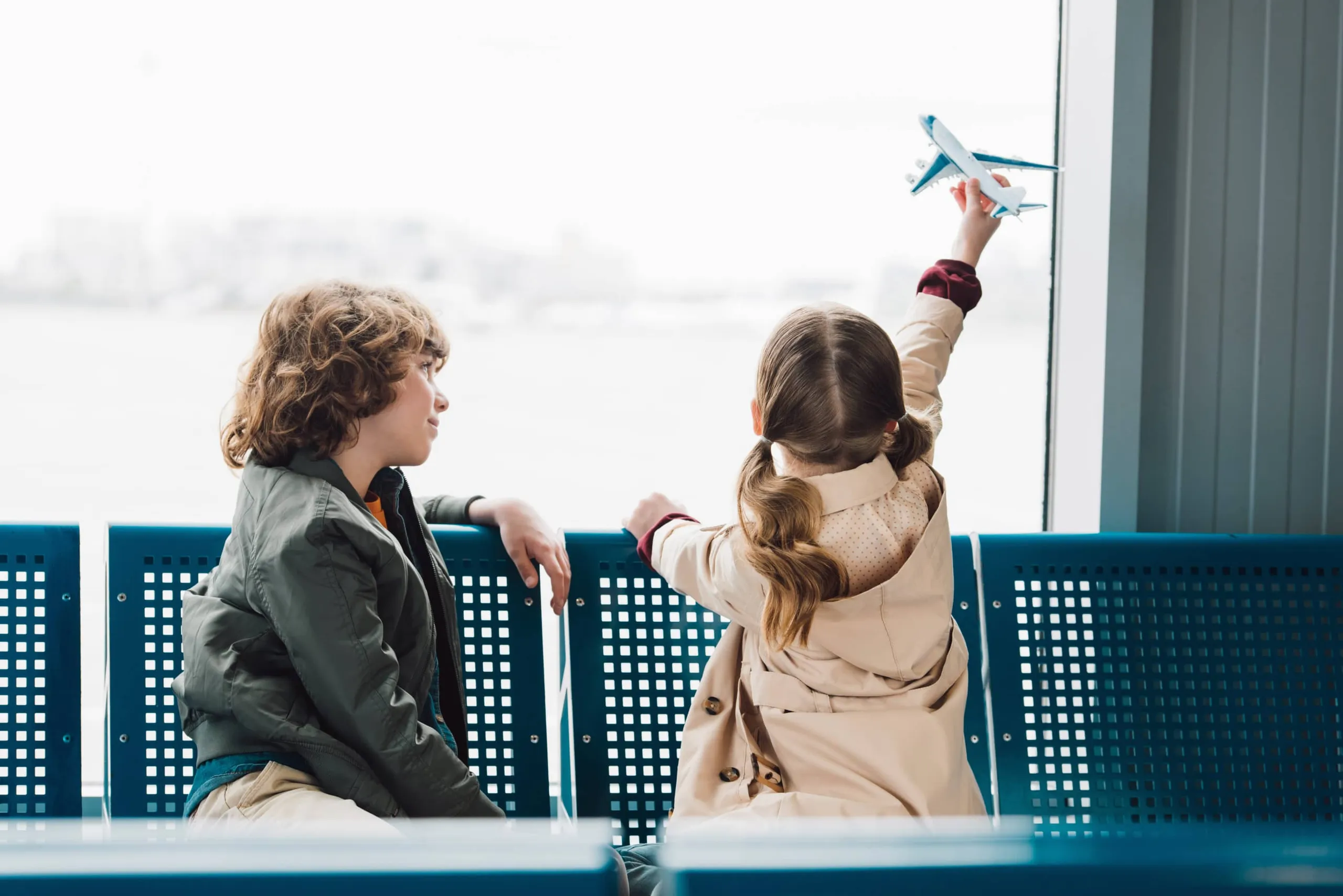 Travel with kids: A little girl flies a toy plane in her hand while a boy waits next to her in the airport.