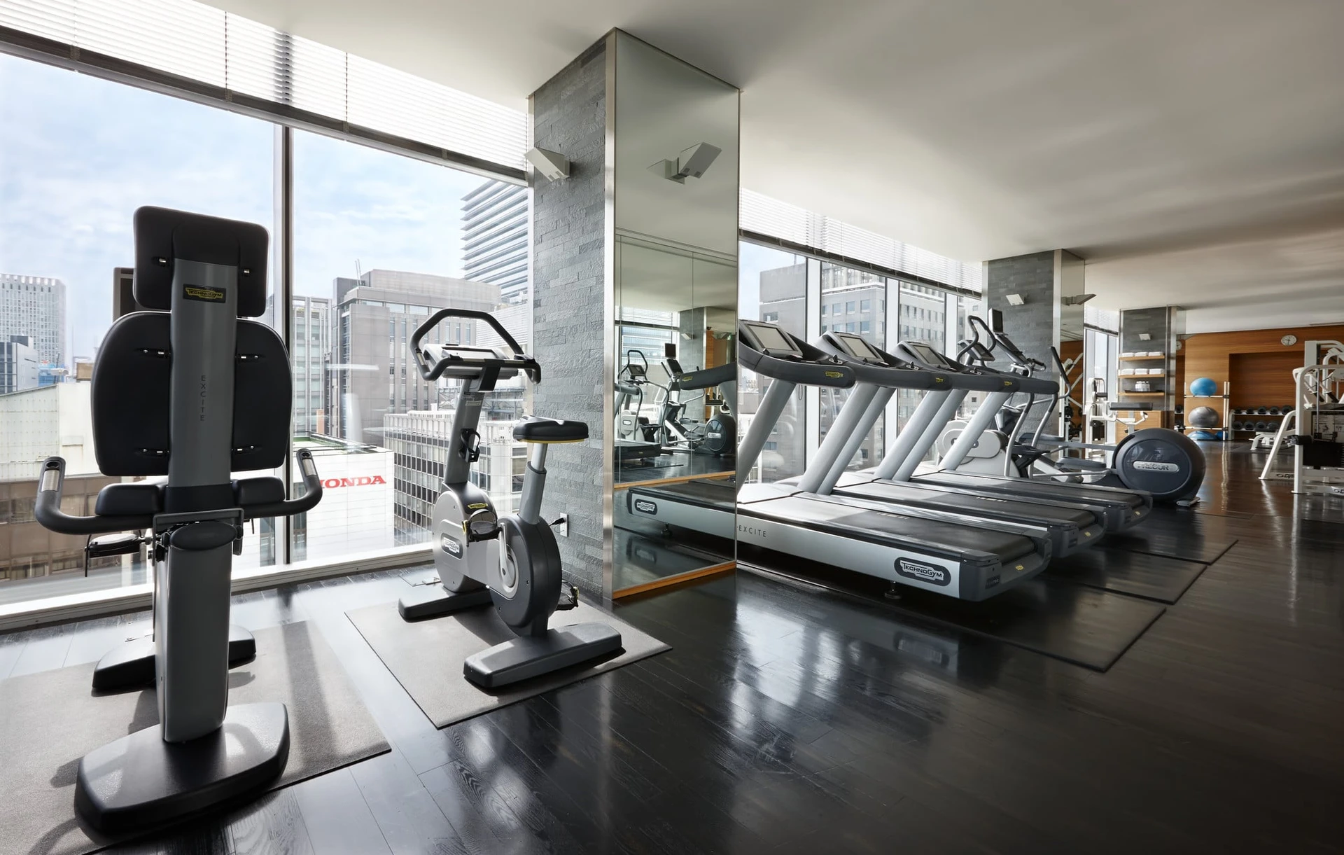 Cardio machines overlooking floor-to-ceiling windows with city views in the fitness center.