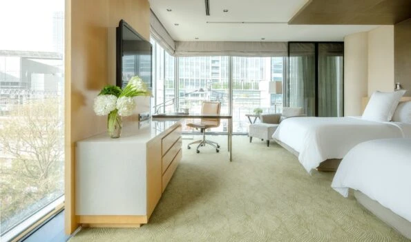 The interior of a Premier Twin corner room features lots of light through the multiple windows, white sheets and a neutral toned desk and seating area.