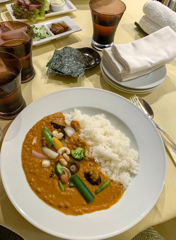 A plate of Japanese curry and rice with perfectly-placed steamed vegetables on top of a room service cart.