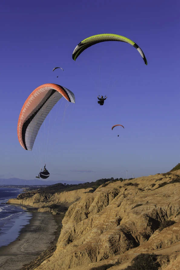 Gliders with colorful parachutes against blue sky and over the bluffs at Torrey Pines Gliderport.