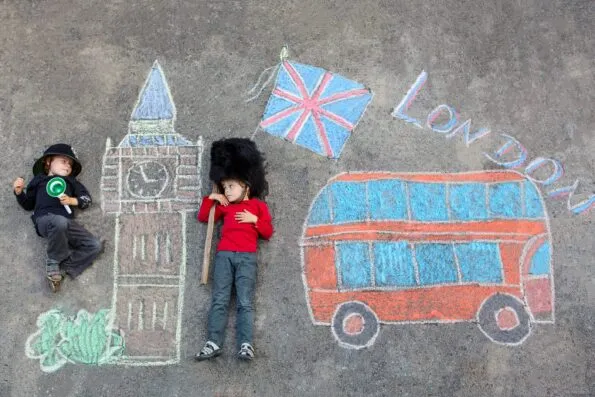 Two funny little friends boys in british queen's guard soldier and policeman uniform having fun with London picture drawing with colorful chalks. With Big Ben, Union Jack and red bus. 