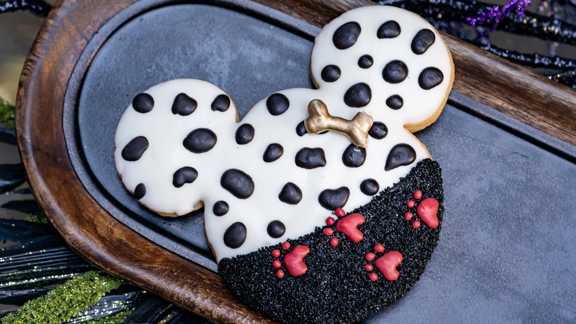 A cookie shaped like a Mickey head with dalmatian spots and red footprints.