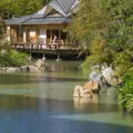 View over the water to the teahouse with a woman in a kimono walking on the terrace.