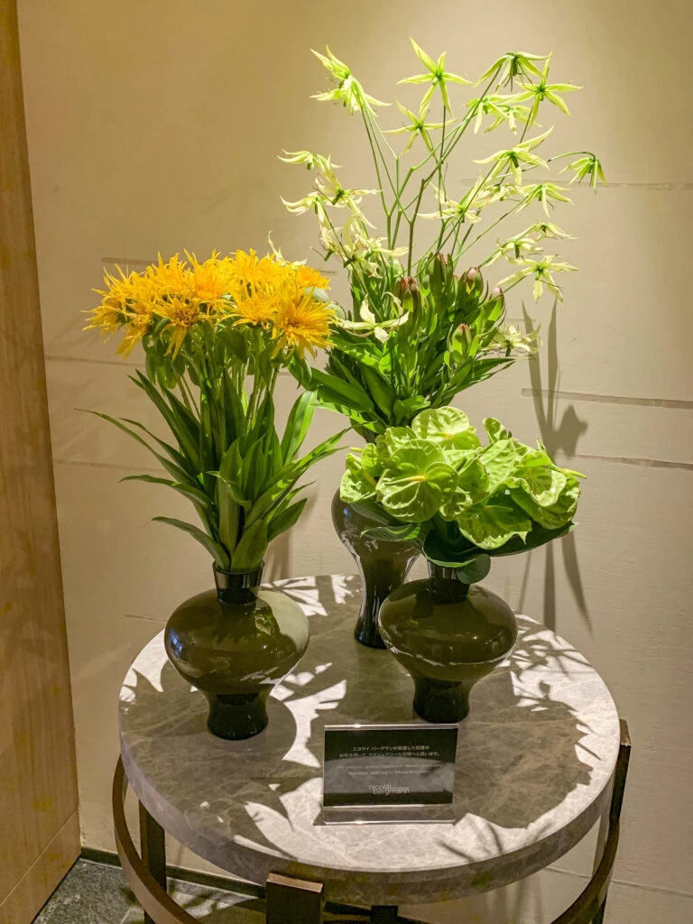 Three vases (two with green flowers and one with yellow flowers) sitting on a table near the spa.