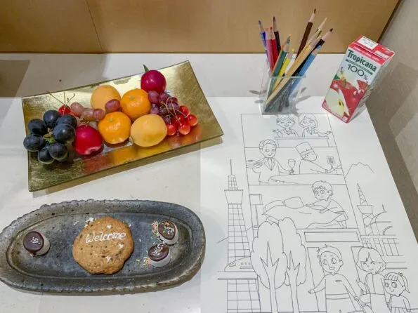 In-room welcome amenities of fruit in addition to a juice box and plate of sweets for kids next to colored pencils and a coloring sheet featuring Tokyo sights.