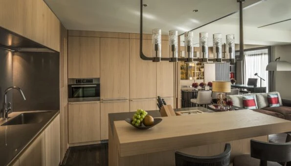 Interior view over the light-colored wood panel kitchen and its kitchen island to the living area and dining room in a Residential Suite.