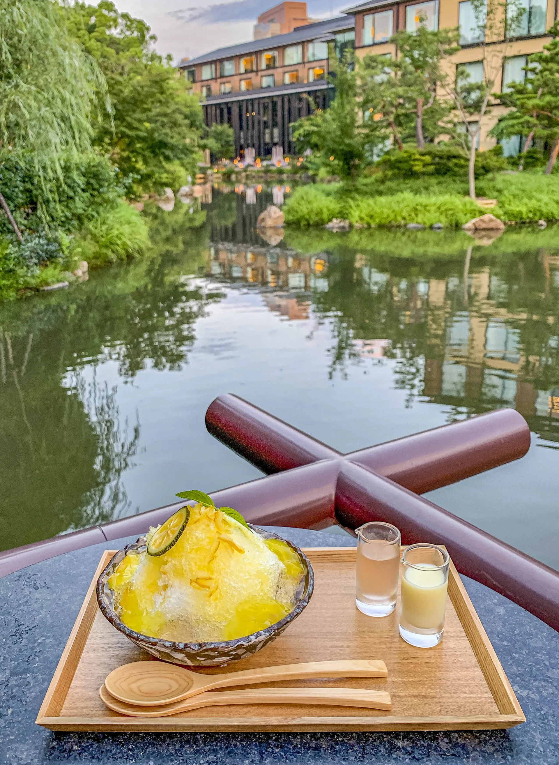 The giant Yuzu Citron shave ice in a bowl on a wood tray with a view of the pond and hotel in the background.