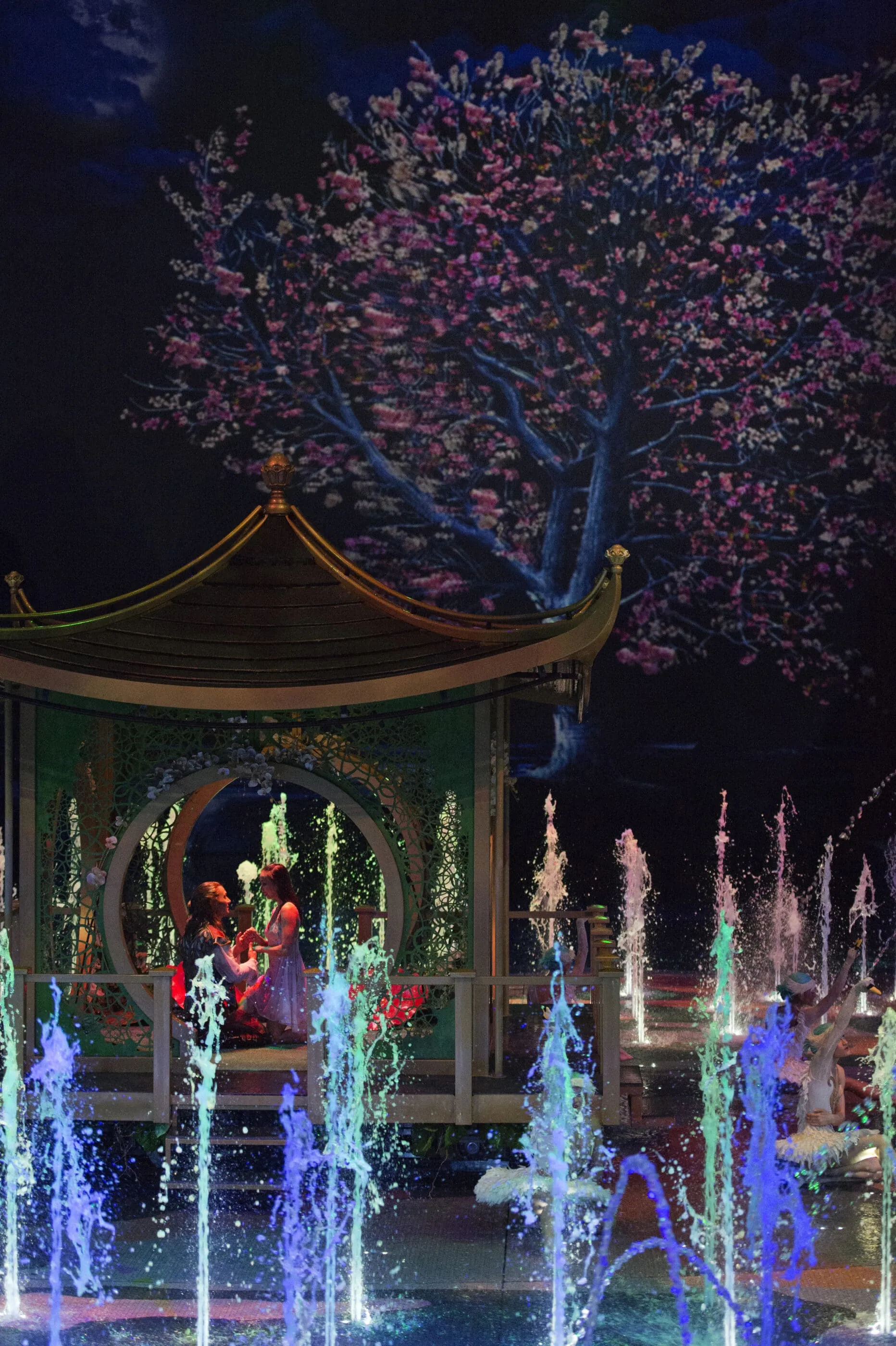 The shipwrecked stranger and woman kneel in a pagoda at the center of the stage with water jets shooting up around them.