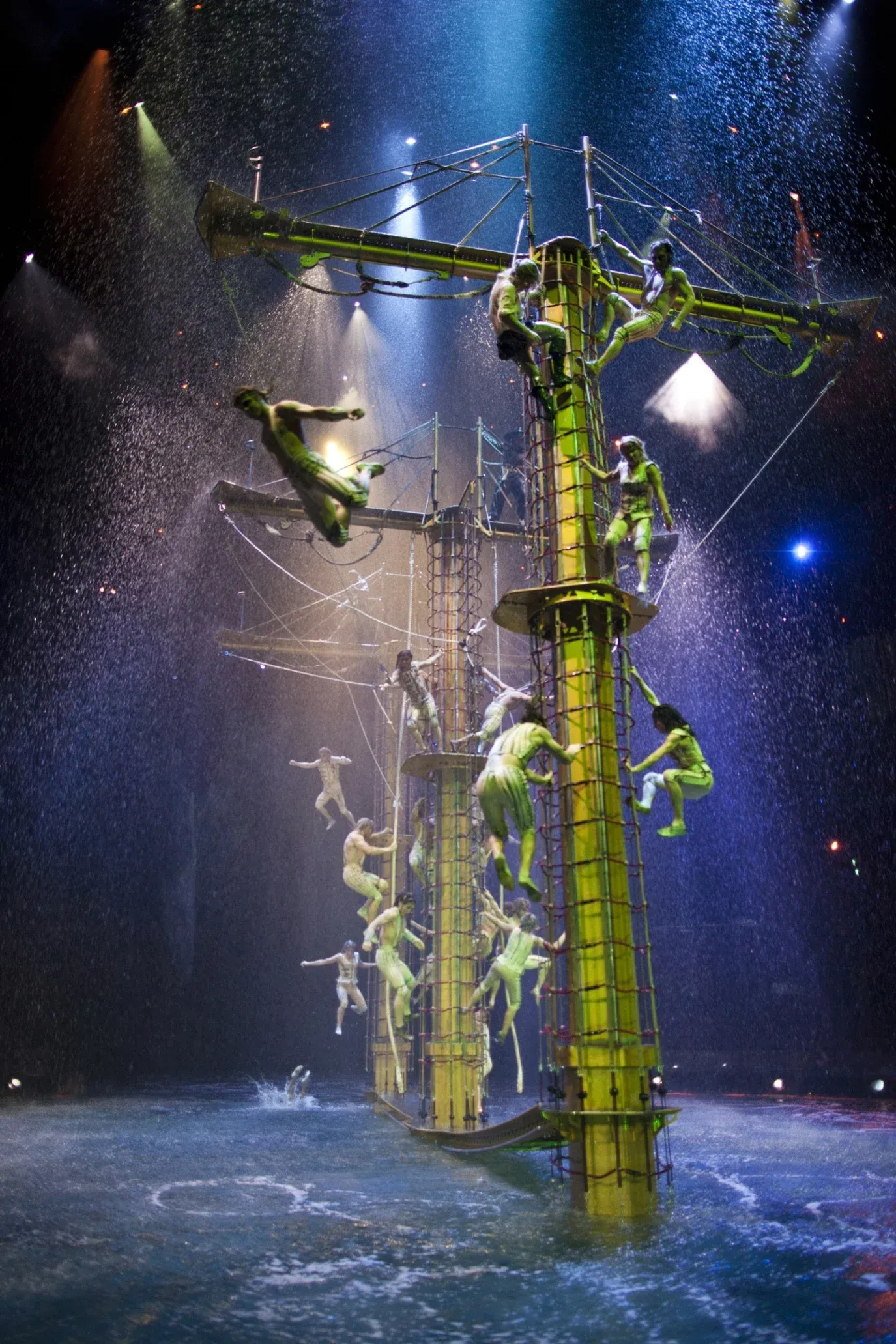 Acrobats climb up a shipwrecked ship surrounded by water on stage.