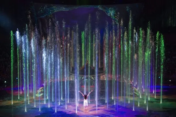 The princess with arms raised appearing to lift water high into the air on stage in front of the pagoda.