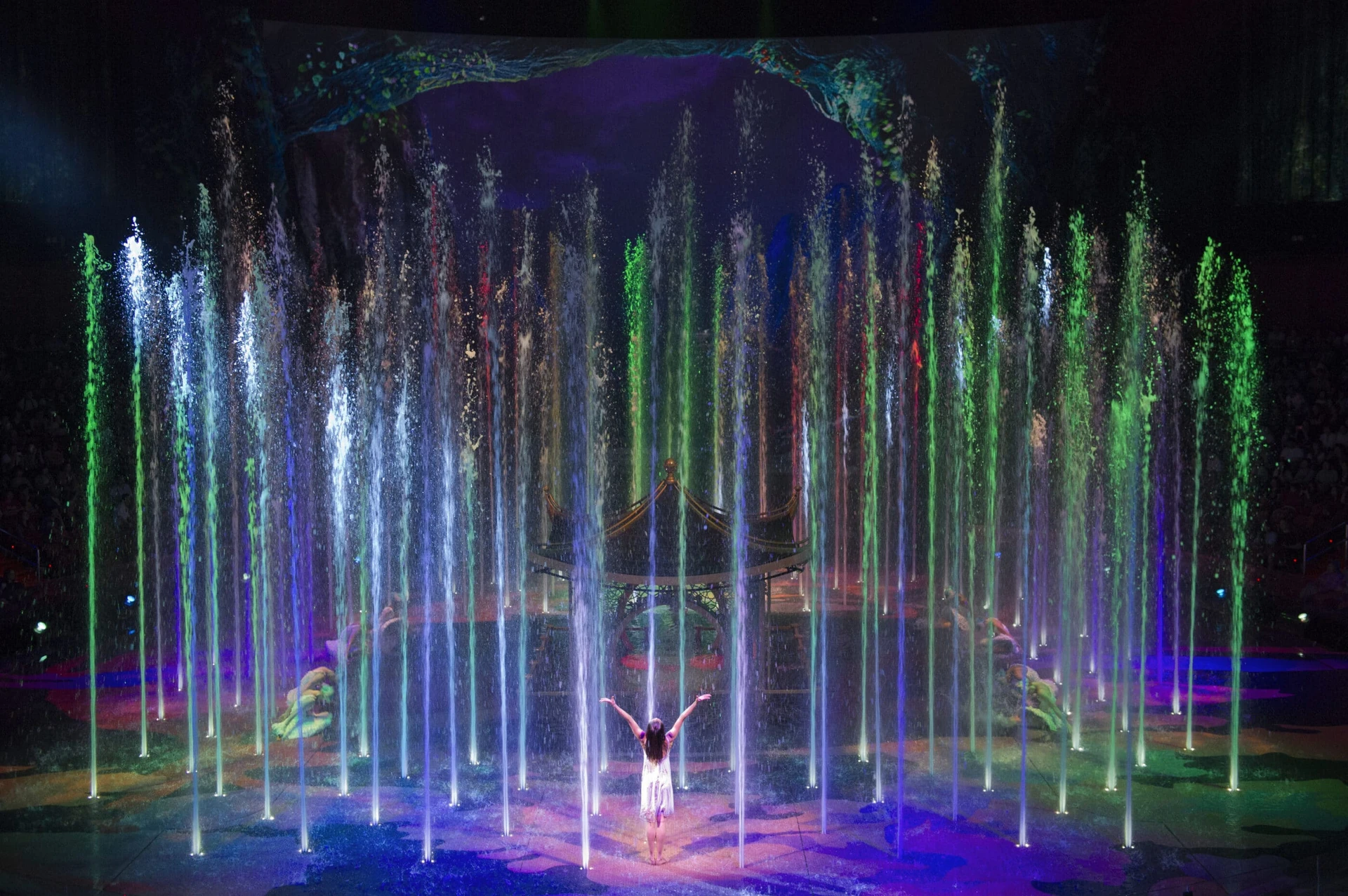 The princess with arms raised appearing to lift water high into the air on stage in front of the pagoda. 