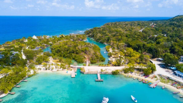 An aerial view of James Bond beach including turquoise water in its inlet, colorful boats docked on the beach, green foliage scattered throughout.