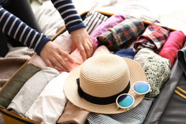 A woman packs clothes and a hat into a suitcase.