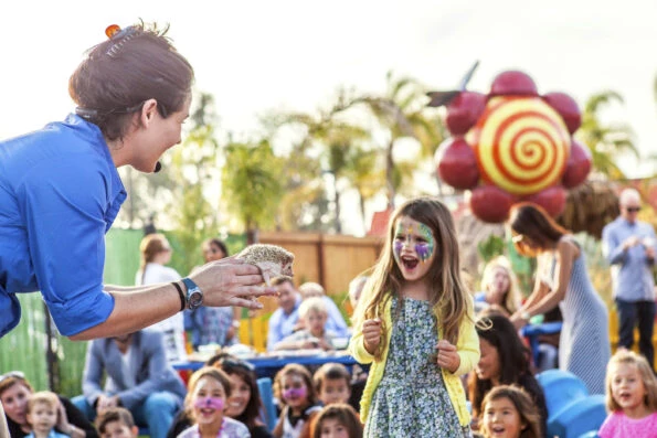 A little girl smiles while looking at a hedgehog held by a museum staff member.