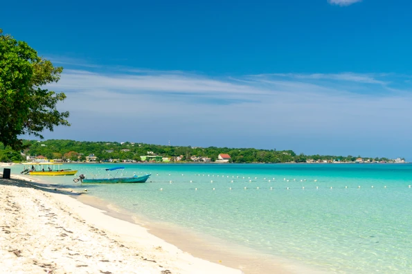 Colorful boats docked in the sand of Seven Mile beach in Jamaica, bordered by stunning turquoise water.