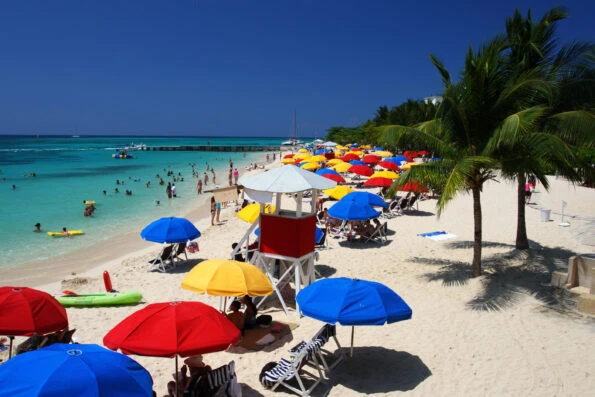 Red, yellow and blue umbrellas dot the beach around a lifeguard tower at Doctor's Cave Beach.