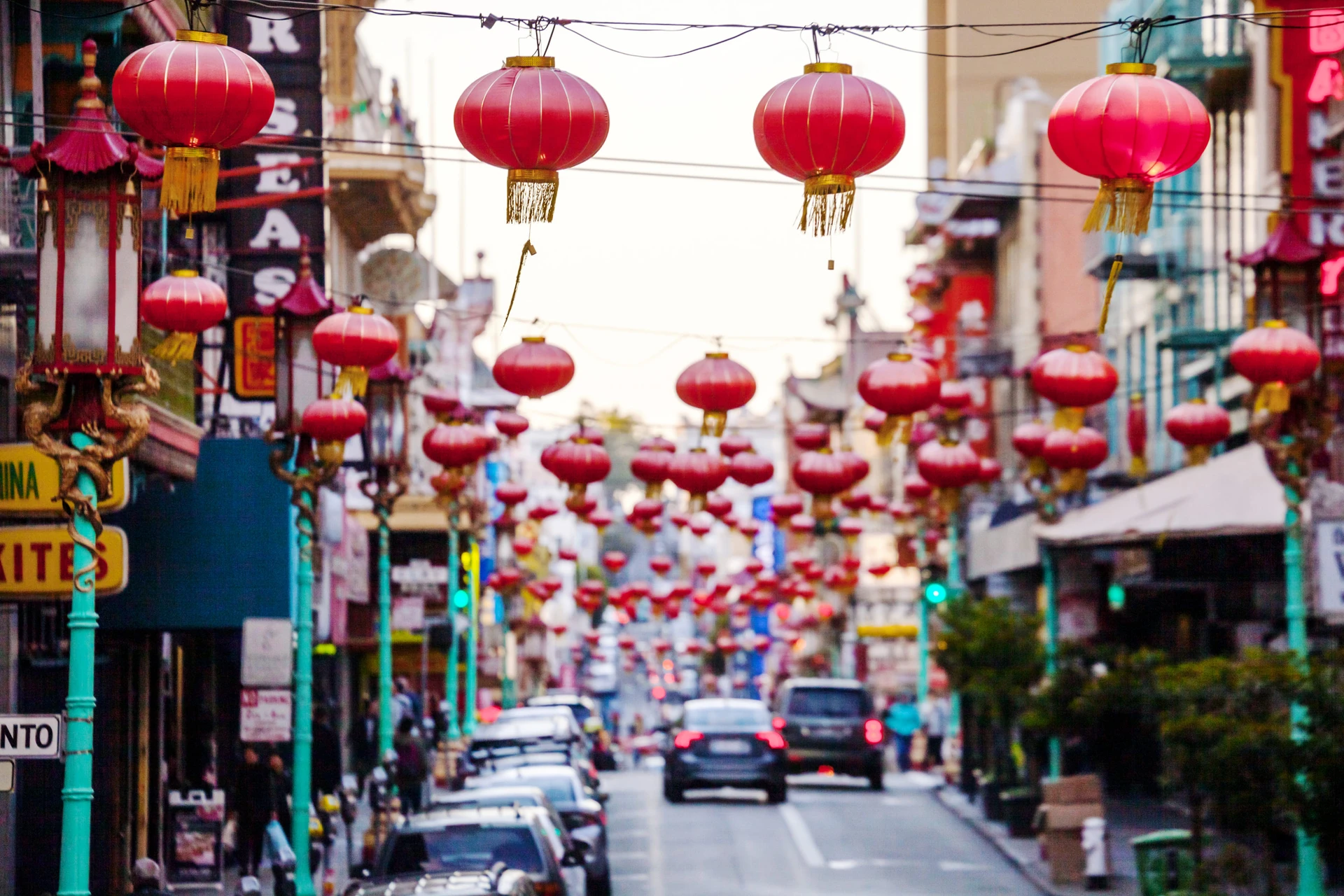Red Chinese lanterns hang over the street with cars driving under them in Chinatown.