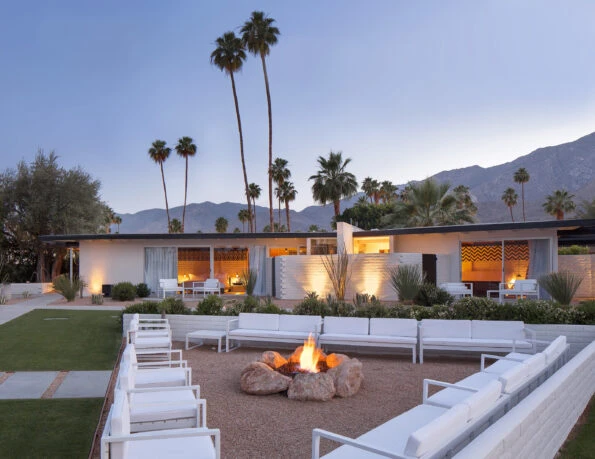 Modern white outdoor lounge chairs in a triangle configuration surround a rock fire pit with the one-story accommodations in the background.