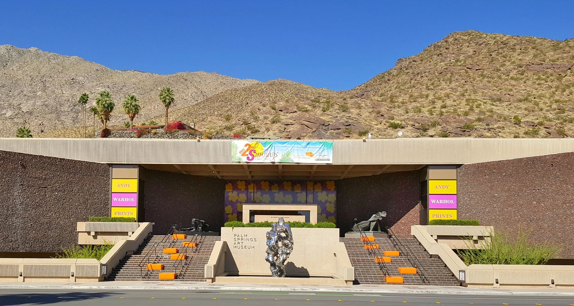 The one-story exterior of the museum with mountains and palm trees in the background.