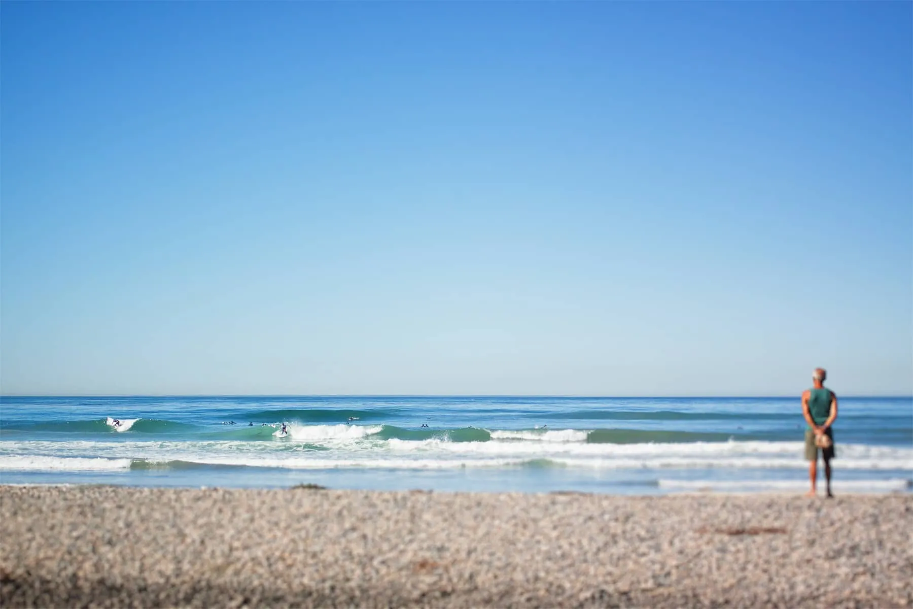 A man stands in the sand and watches surfers at Del Mar beach.