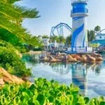 A lighthouse in the middle of a lake with a rollercoaster behind it.
