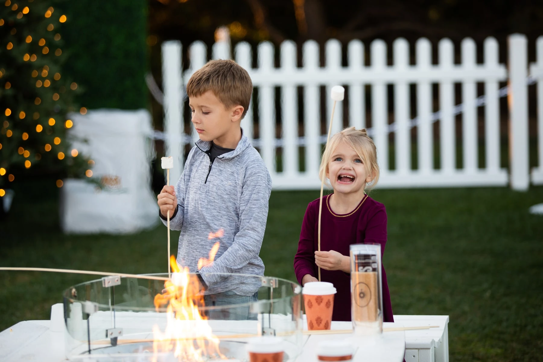 Two small children roast s'mores at a table.