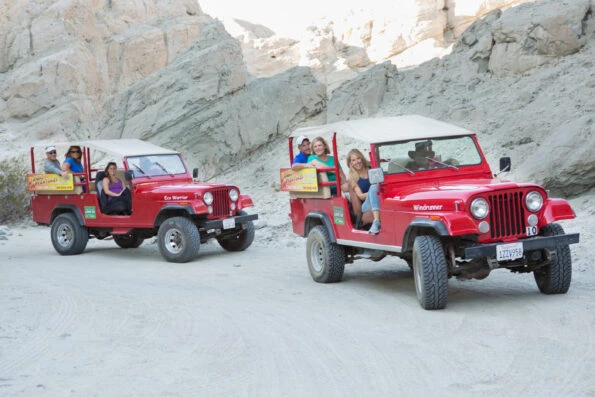Two red Jeeps full of guests off-road in the desert.
