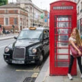Girl in front of a red British phone booth as a traditional black taxi passes by.