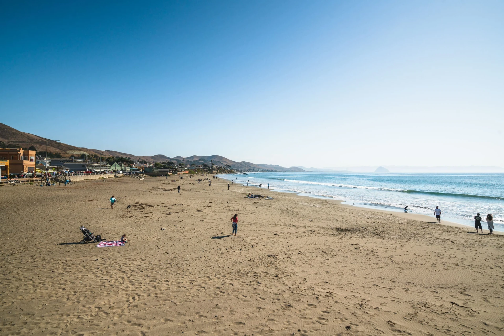 People sitting on the sand and walking along the shoreline of Cayucos State Beach.