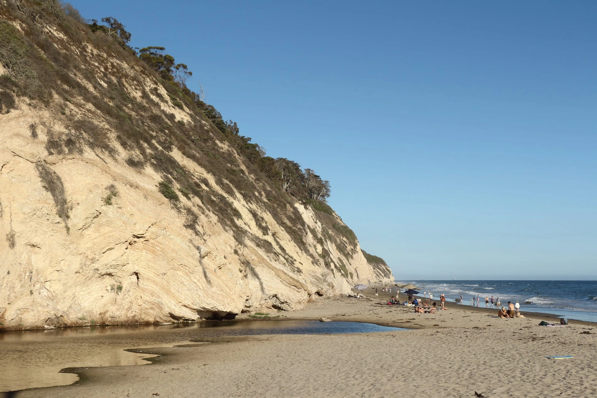 People walking the beach next to tall cliffs at Arroyo Burro beach in Santa Barbara, a popular California family beach.