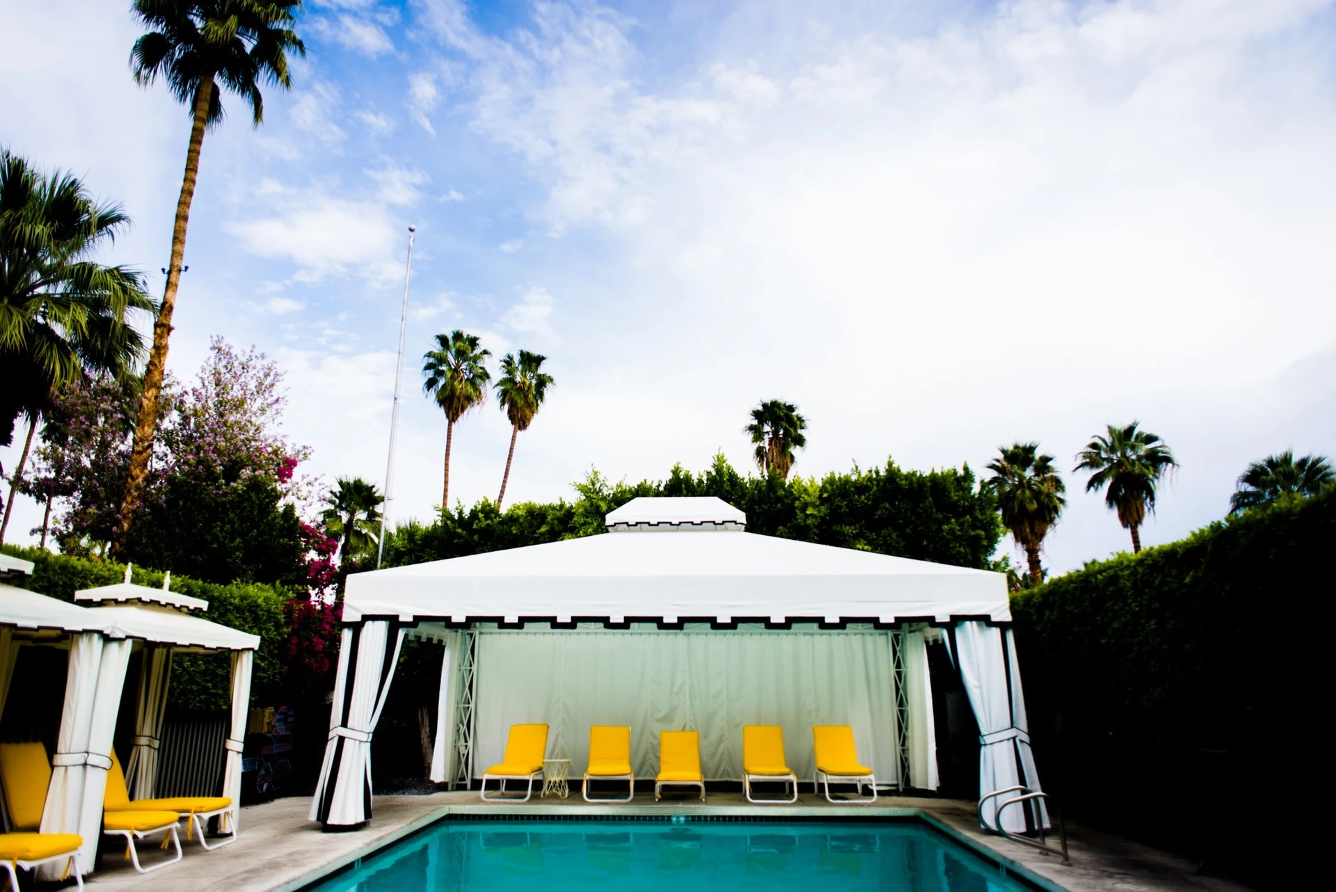 Yellow lounge chairs under a white canopy with black trip next to the pool at Avalon Hotel and Bungalows.