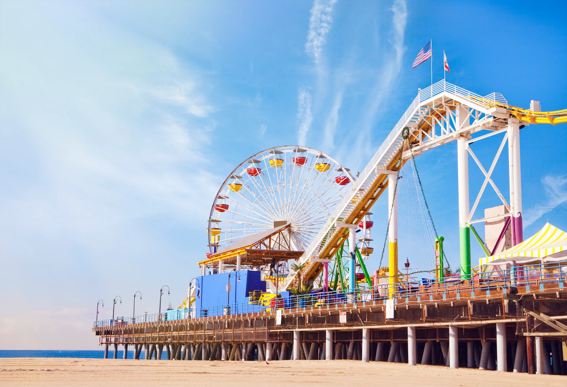 A view from the sand to the Ferris wheel and carnival activities at the end of the Santa Monica Pier.