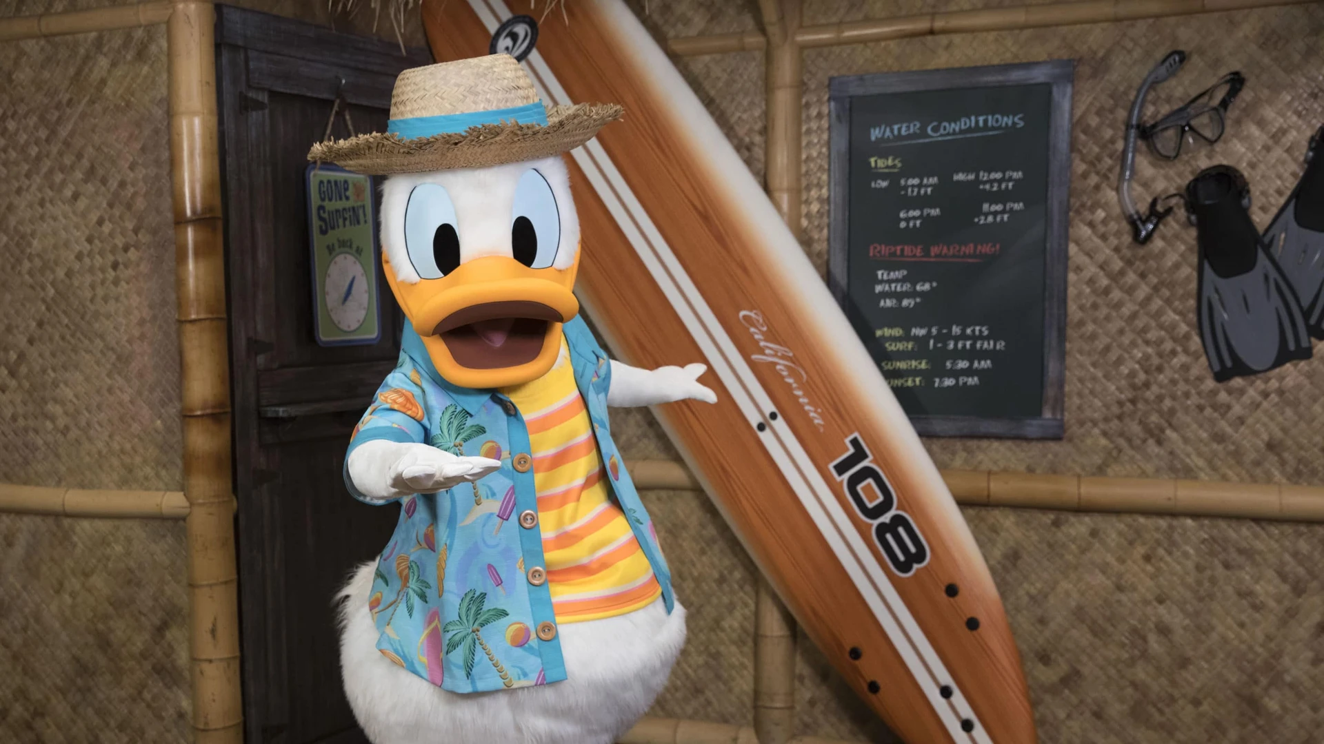 Donald Duck poses in vacation wear next to a surfboard at 