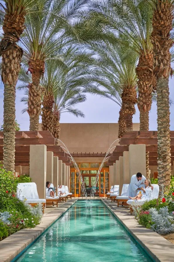 Couples relax next to a spa water feature outside under palm trees at Hyatt Regency Indian Wells.