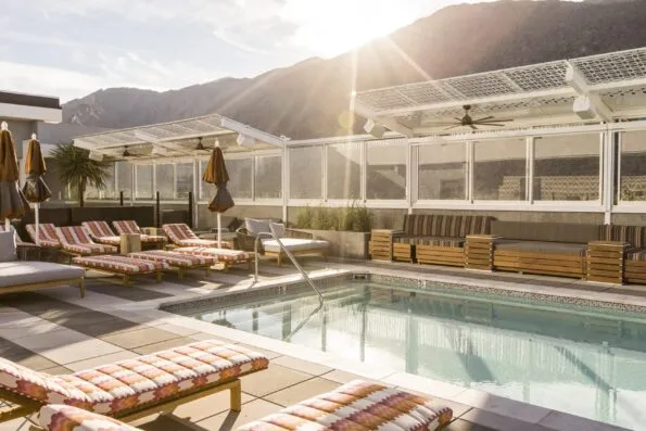Morning sun over the mountains shines on the Kimpton Rowan pool deck lined with empty lounge chairs.