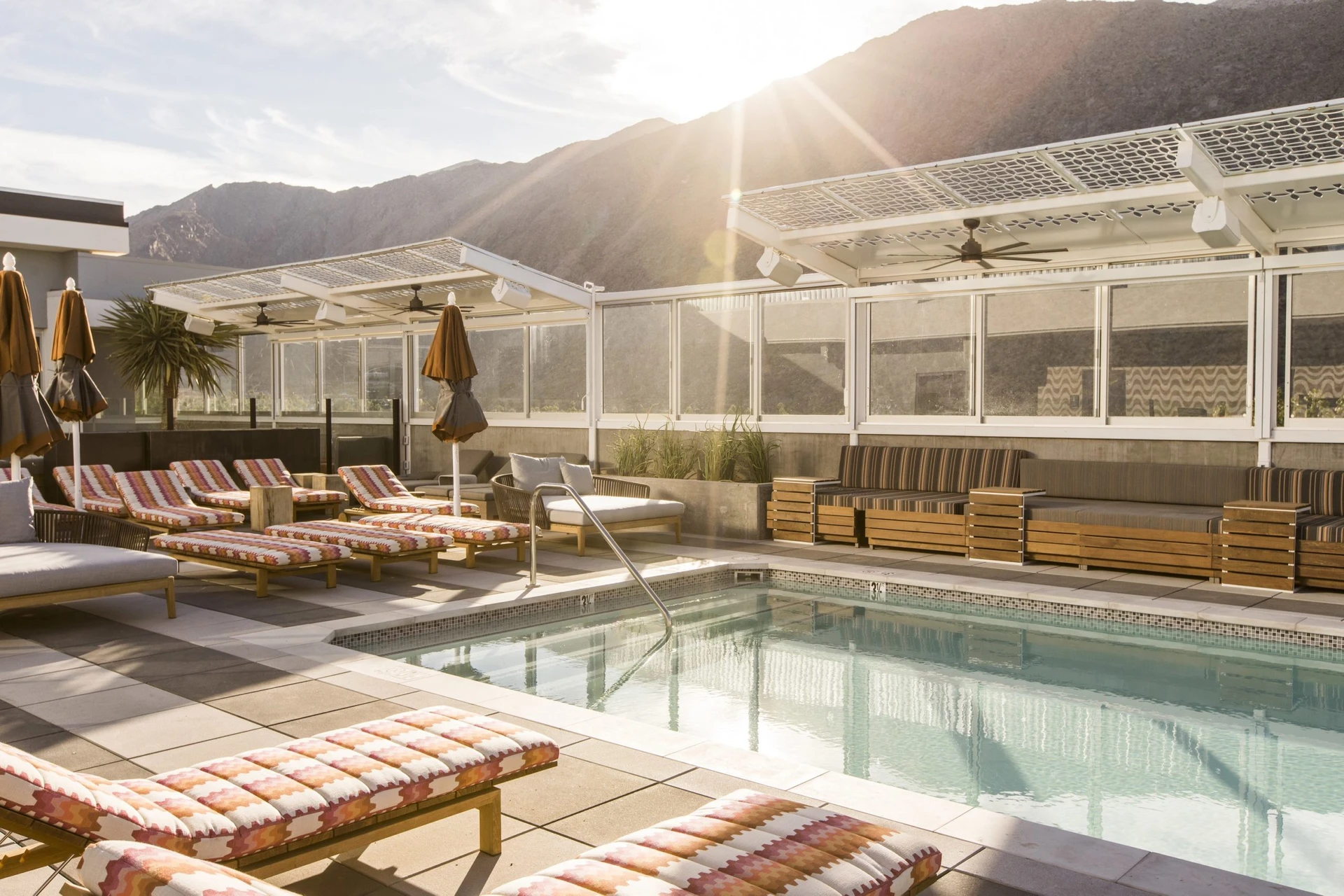 Morning sun over the mountains shines on the Kimpton Rowan pool deck lined with empty lounge chairs.