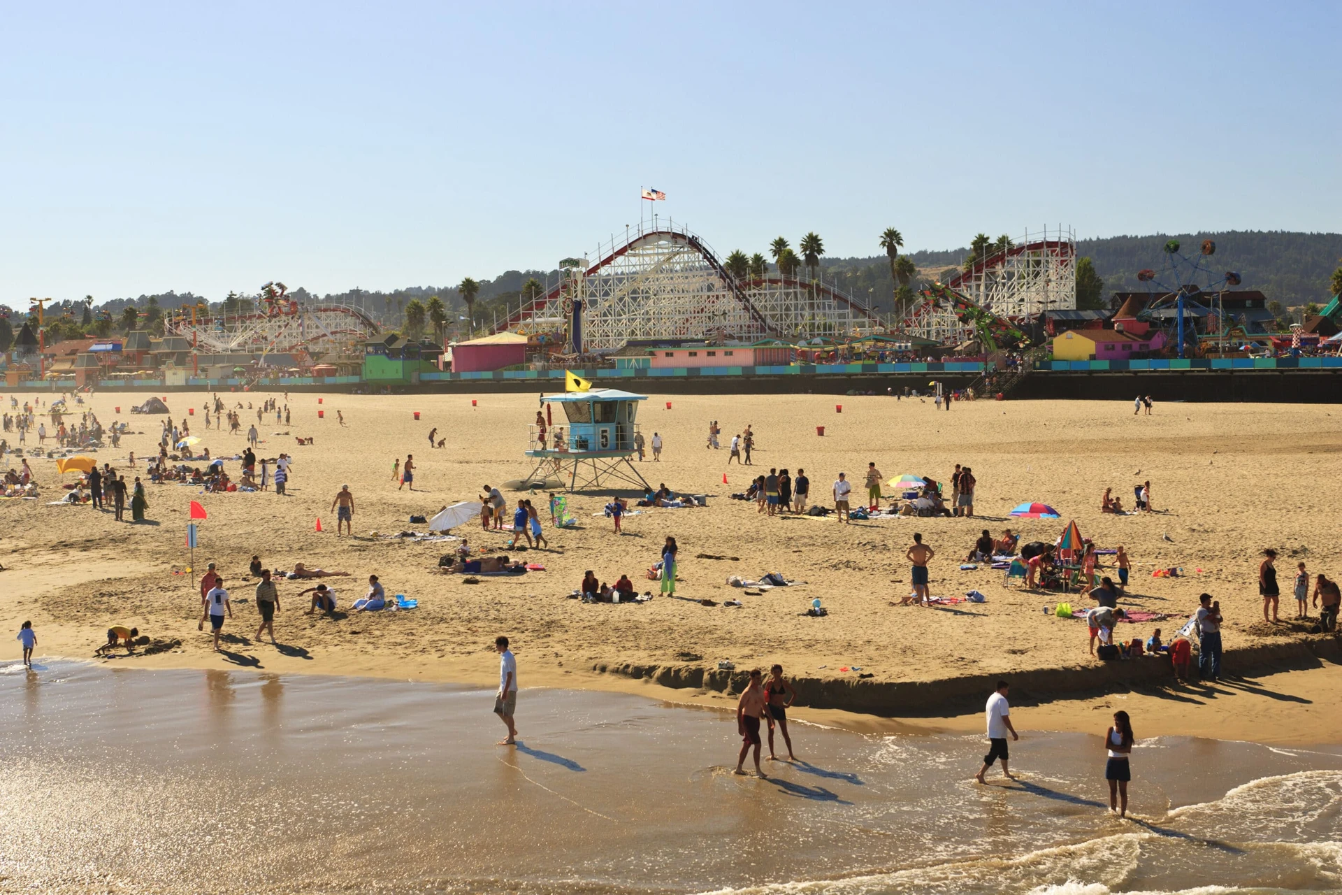 People enjoying the Santa Cruz beach with the boardwalk rollercoaster in the background.
