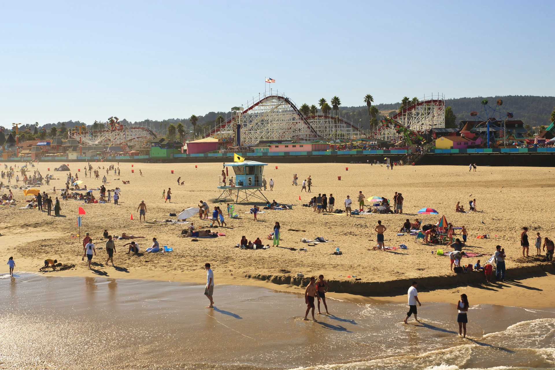 People enjoying the Santa Cruz beach with the boardwalk rollercoaster in the background.