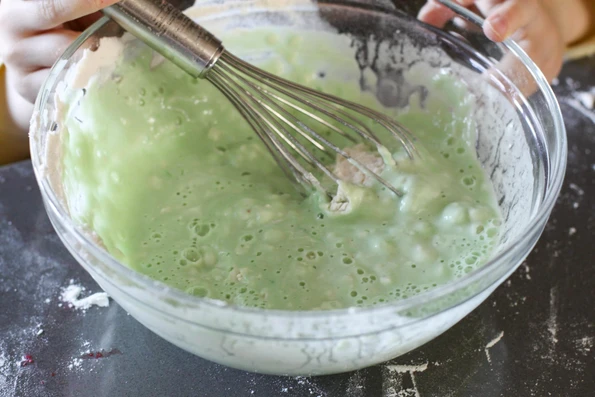 Whisking lumpy green cold water finger paint together in a glass bowl.