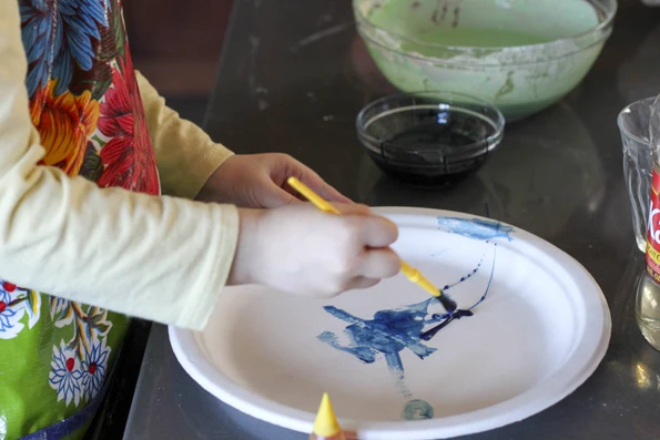 My daughter paints with blue cornstarch finger paint on a paper plate.