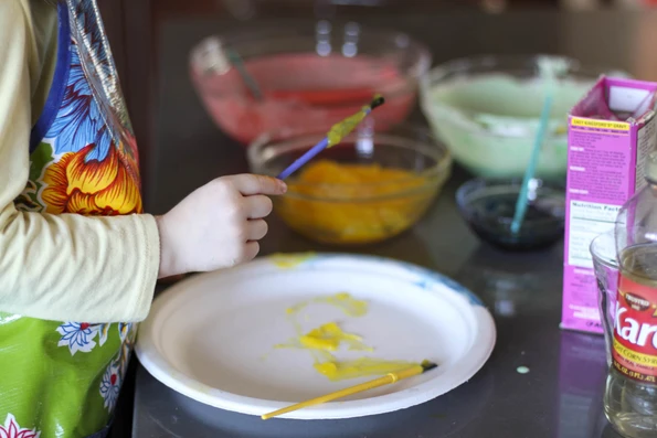 Painting yellow cornstarch finger paint recipe on a paper plate.