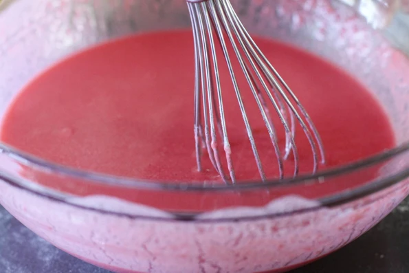 Whisking red Kool Aid finger paint recipe together in a glass bowl.