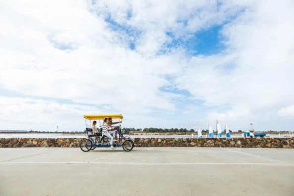 A family in a surrey bike rides down the boardwalk along Mission Bay in front of the resort.